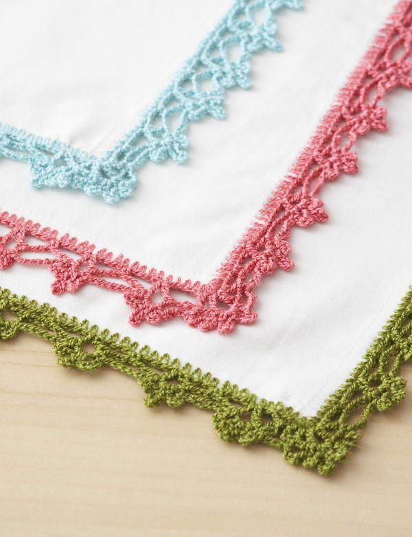 Image shows the Lace Napkin Edging design: three napkin corners with lace borders in blue, pink, and green.