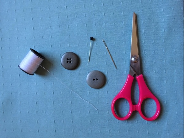 Image shows the materials needed to sew a button: thread, needle, pin, button, and scissors.
