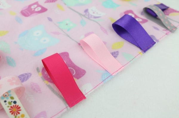 Image shows a close up of the blanket fabric with folded ribbons sewn on the edge.