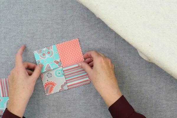 Image shows hands holding the four rectangle fabric pieces to make the square folded fabric coaster folded properly on a gray background.