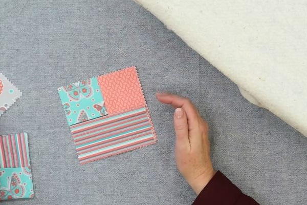 Image shows hands arranging three rectangle fabric pieces to make the square folded fabric coaster on a gray background.