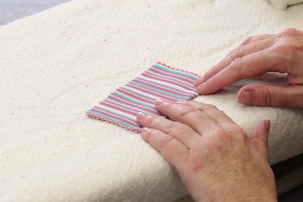 Image shows hands pushing down a rectangle piece of fabric on an ironing board.