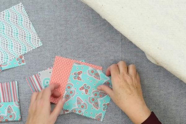 Image shows squares of fabric on a gray background. Hands are arranging them.