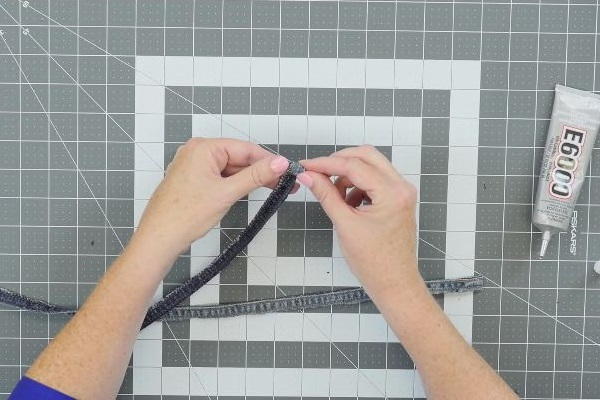 Image shows a cutting mat background with hands rolling the jean fabric strip.