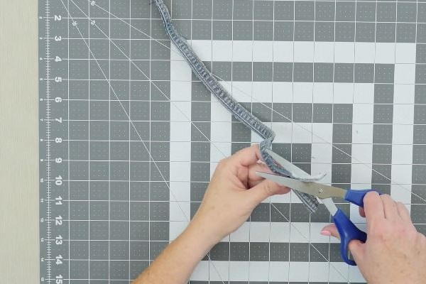 Image shows a cutting mat background with two hands cutting the seam from a pair of jeans.
