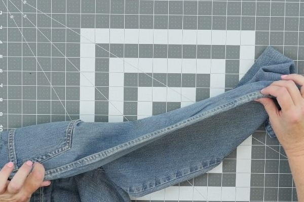 Image shows a cutting mat background with two hands holding the with the double-stitched seam side of a pair of jeans.