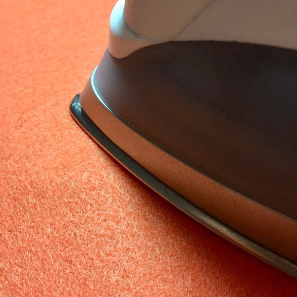 An image of an iron working the creases out of orange felt