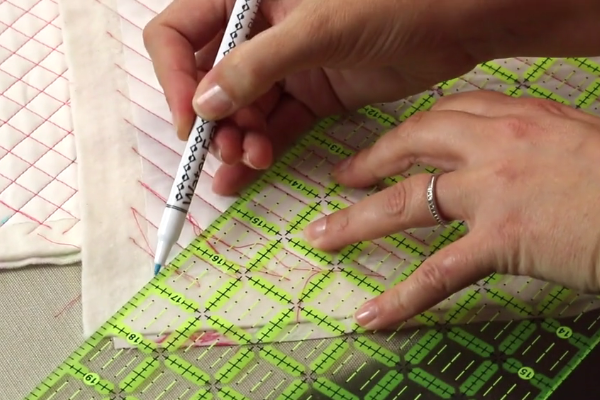 Image shows a person using a ruler and a fabric marking pen to mark lines on the fabric swatch.
