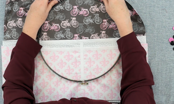 Image shows hands adjusting the outer embroidery hoop over another set of fabric pieces (the pockets).