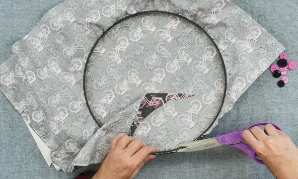 Image shows hands cutting off the excess fabric from the back of the embroidery hoop organizer.
