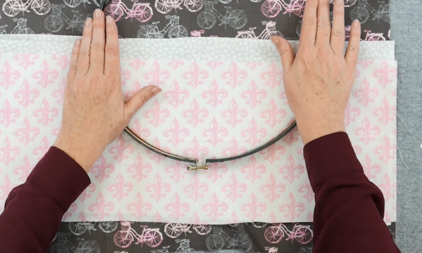 Image shows hands pushing the outer embroidery hoop over another set of fabric pieces (to be the pockets).
