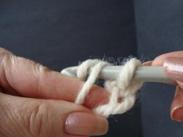Image shows step 6 for crocheting a magic ring, which shows a hand holding yarn. There's a hook in the other hand pulling the yarn through to make a single crochet stitch.