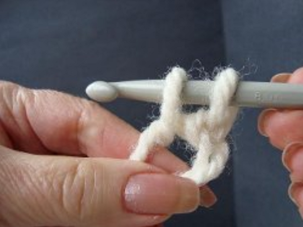 Image shows step 7 for crocheting a magic ring, which shows a hand holding yarn. There's a hook in the other hand pulling the yarn through to make a single crochet stitch.