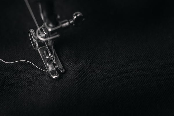 Image shows a close-up of a sewing machine sewing black fabric.