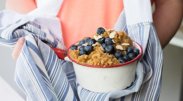 Image shows a close-up of a person wearing the DIY kitchen scarf and holding a pot of blueberry crumble.