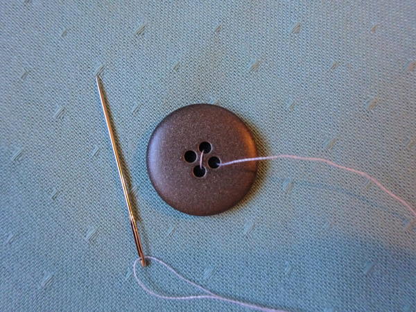 Image shows the button on fabric with one pass of the needle and thread complete.