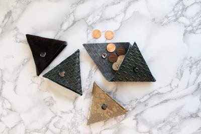 Image shows a gray and white marbled background and four No-Sew Triangle Coin Purses. One is open and coins are spilling out.