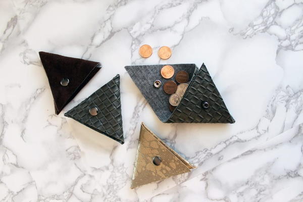 Image shows four of the no-sew triangle coin purses on a light marbled background. One is open and has coins falling out of it.