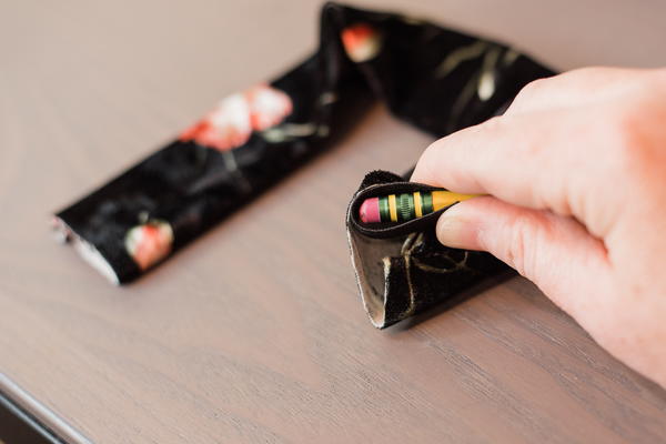 Image shows a pencil with elastic wrapped and held over the eraser, about to be inserted into the scrunchie tube.