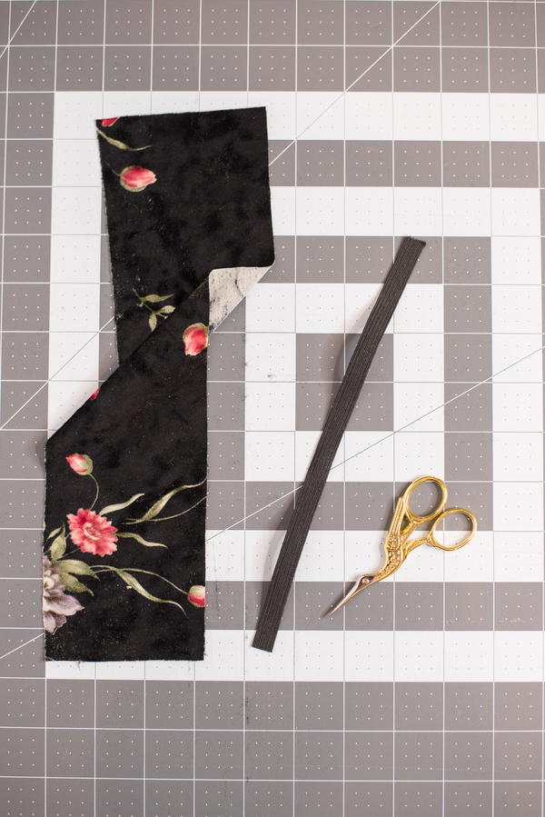 Image shows a piece of fabric, length of elastic, and scissors sitting atop a cutting mat.