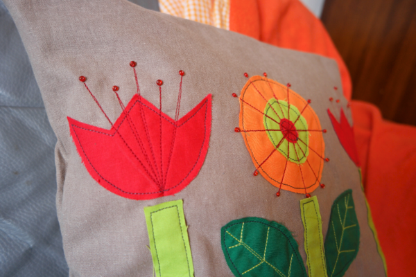 Image shows a close up of the flowers on the finished cushion sitting on a chair with a red blanket draped over the back and seat.