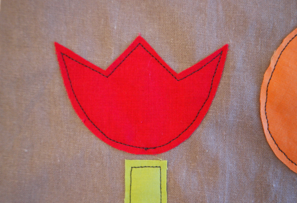 Image shows close-up of a red embroidered flower on the cushion. How to Applique Flowers to the Cushion - Step 1