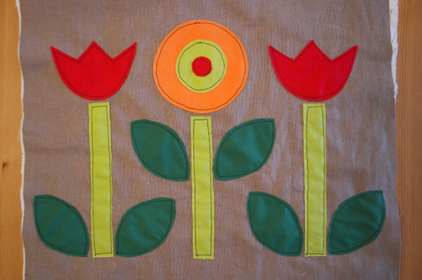 Image shows close-up of three embroidered flowers with dark green leaves on the cushion. How to Applique Flowers to the Cushion - Step 4