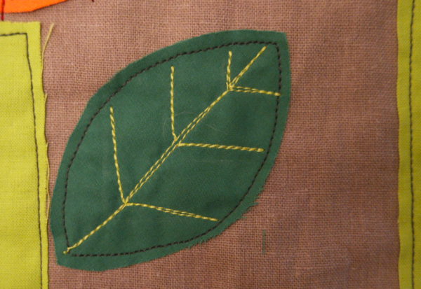 Image shows close-up of a dark green embroidered leaf with vein accent lines, on the cushion. How to Embroider the Flowers - Step 4
