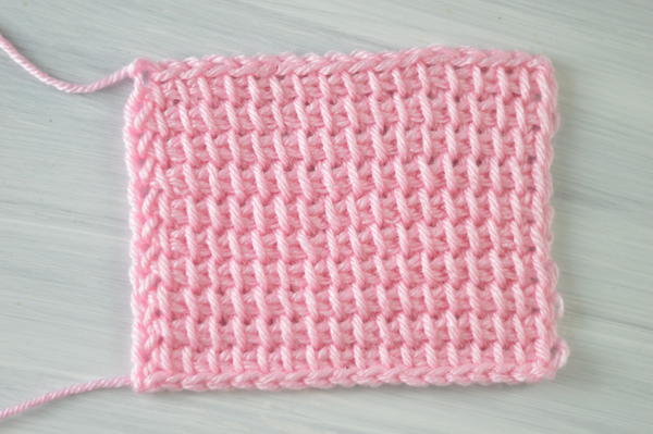 Image shows a rectangle swatch in pink showing the Tunisian crochet simple stitch.