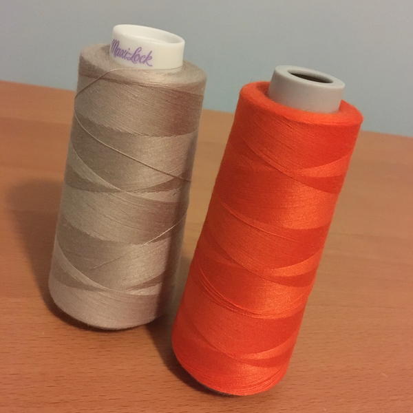 Image shows two spools of thread used for sergers set upright on a wood surface.