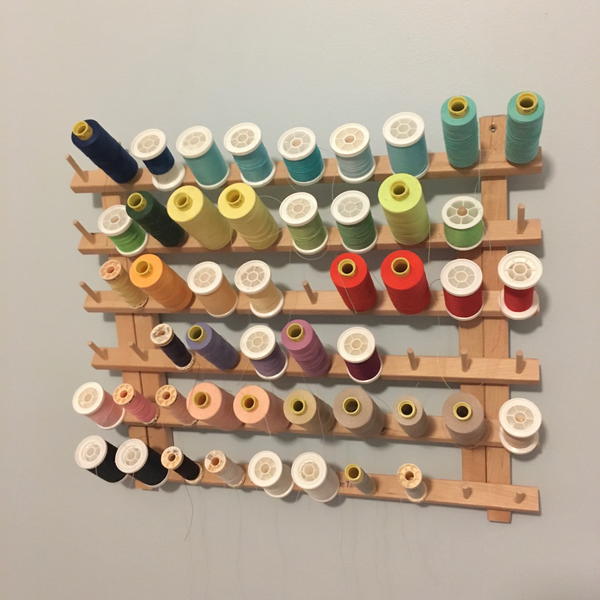 Image shows a thread holder on a wall with various spools of thread attached.