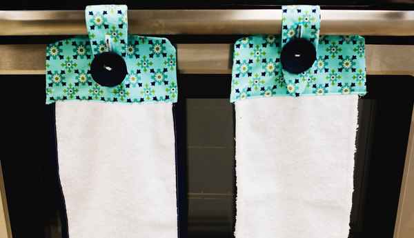 Image shows two finished towels hanging side-by-side on the handle of a stove.