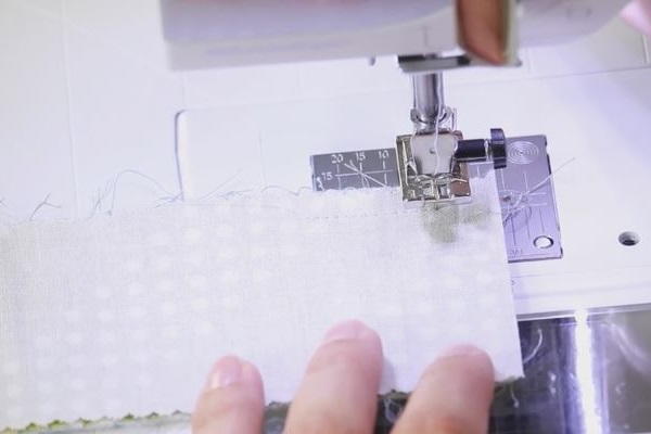 Image shows hands pushing fabric through a sewing machine.