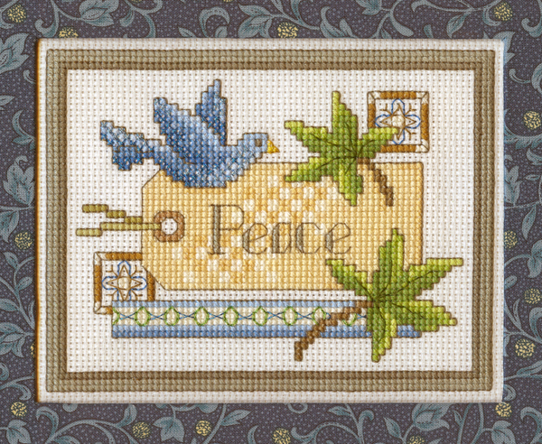 Image shows a Beautiful Peace Label cross-stitch design. There is a stitched gift tag that has "Peace" written on it. There are leaves and a blue bird.