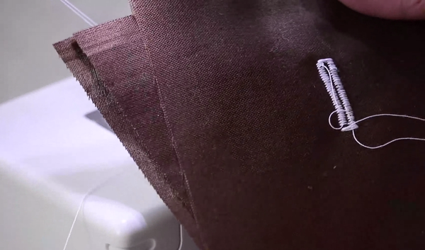 Image shows layered brown fabric in front of a sewing machine with a white buttonhole sewn in the center.