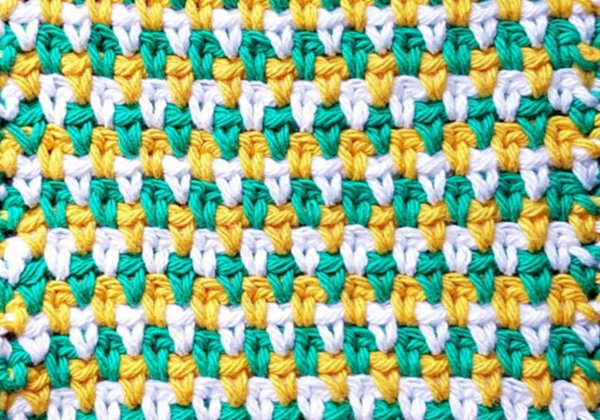 Image shows a close up of a crochet seed stitch swatch in yellow, teal, and white.