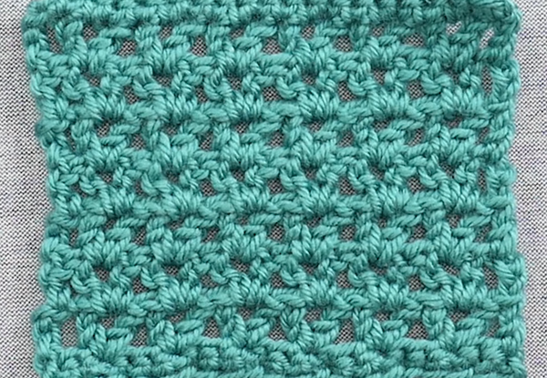 Image shows a close up of a v-stitch crochet swatch in teal yarn. There is a gray background.