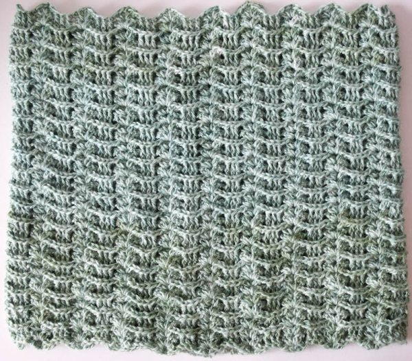 Image shows a textured wave crochet stitch swatch in a muted blueish-green. It is on a light gray background.
