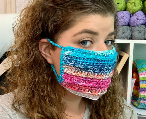Image shows a woman wearing a colorful crochet mask. Image shows a woman wearing a colorful crochet mask.