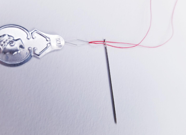 Image shows a needle threader with the needle and red thread attached on a light background.