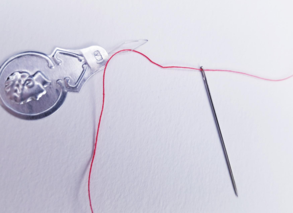Image shows a needle threader with the needle and red thread attached on a light background.