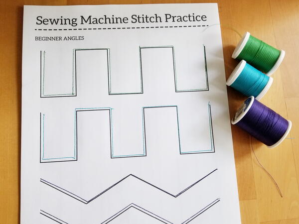 Image shows a sewn practice sheet with three spools of thread to the right of the sheet.