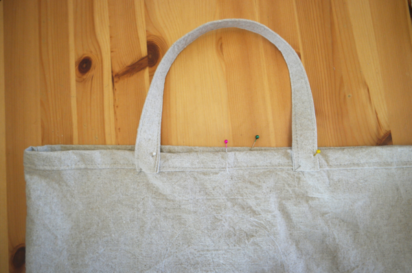 Image shows a close-up of the bag with finished handles sewn on the bag, sitting on a wood table.