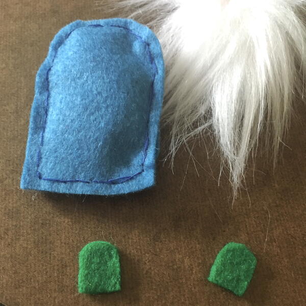 Image shows the blue felt body stuffed and sewn along with two green shoe pieces and the white beard for the DIY Gnome Ornament.