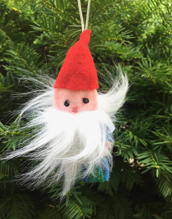 Image shows the finished gnome ornament hanging from an evergreen tree outside.