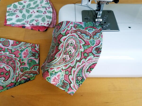 Image shows a sewing machine sewing two sides of a DIY face mask together. Off to the side, there are mask pieces sewn and waiting to be sewn.