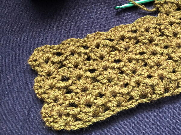 Image shows a close-up of the start of a shell stitch blanket in gold.