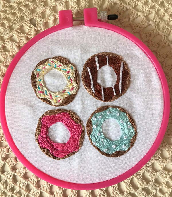 Example of hand embroidery: four hand embroidered donuts in a pink embroidery hoop.