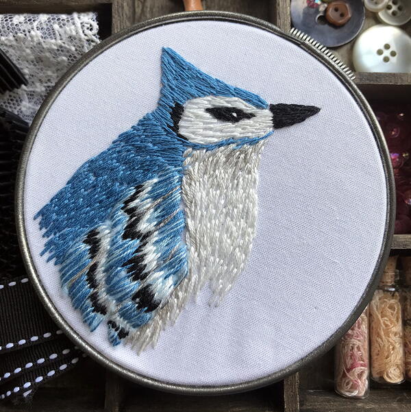 Example of needle painting embroidery: an intricate blue jay in a silver embroidery hoop.