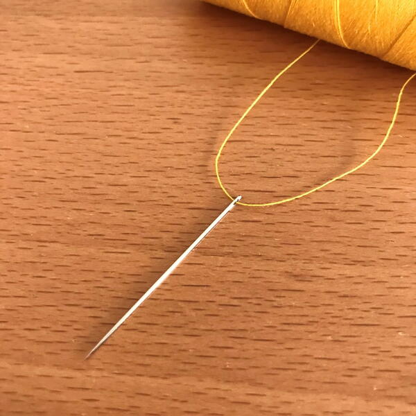 Image shows a hand sewing needle threaded.